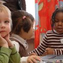 Children sitting at a table. One child is wearing a headset.