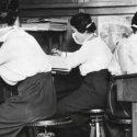 Three masked women working at desks, c 1918-1920